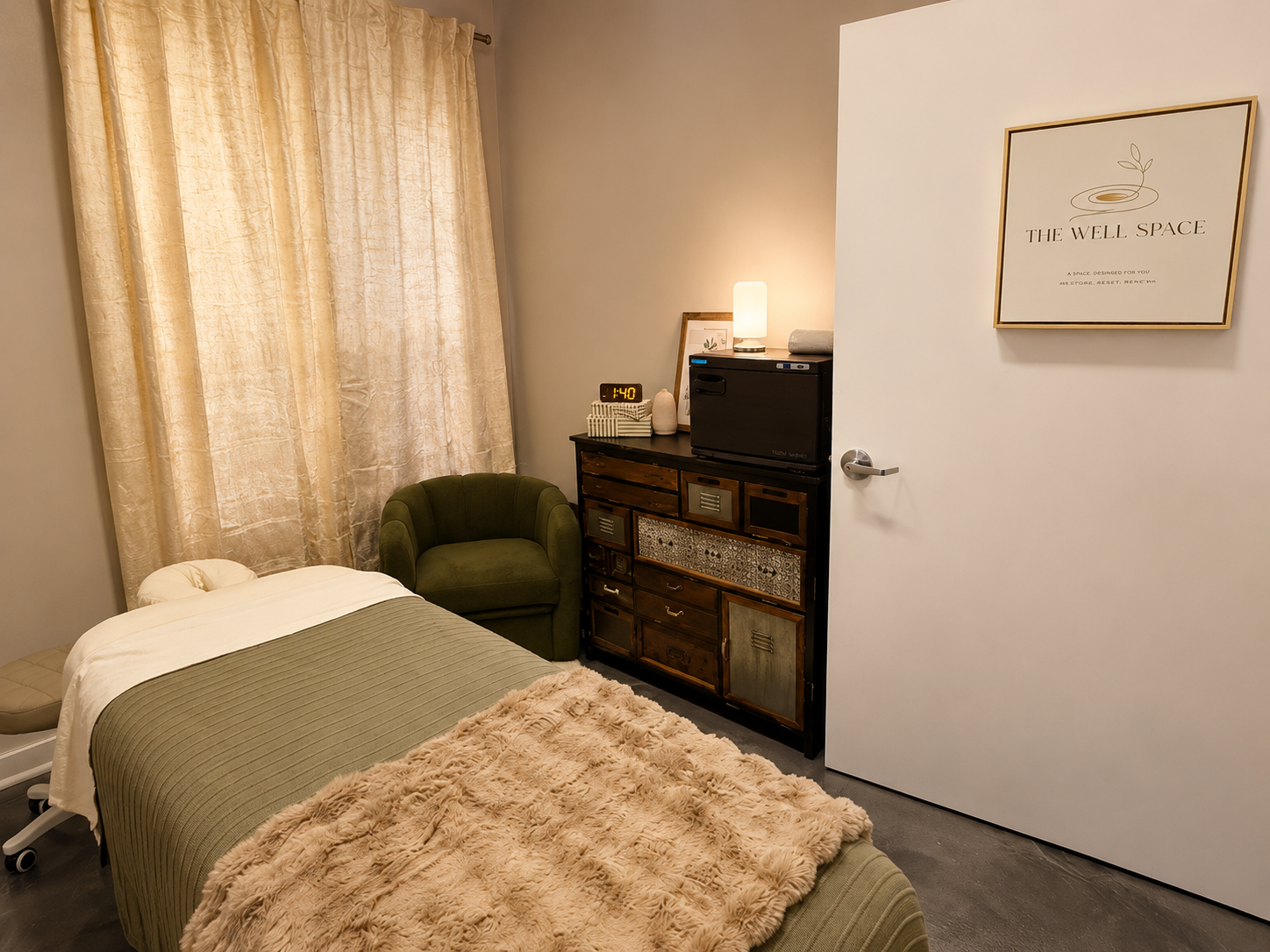 The Well Space treatment room in Tampa, with a draped massage table, warm lamplight, and the studio's framed logo on the door.